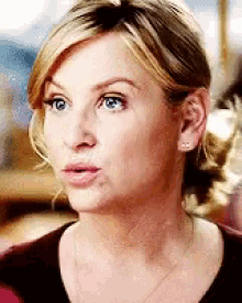 a woman with blonde hair and blue eyes is wearing a brown shirt and a necklace .