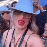 a woman wearing a cowboy hat , sunglasses and a necklace is sticking her tongue out .