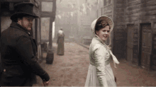 a man in a top hat and a woman in a green dress walk down a dirt road
