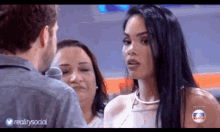 a woman is talking to a man in front of a microphone while another woman looks on .