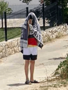 a person is standing on a sidewalk with a towel covering their face .