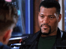 a man with a beard is wearing a leather jacket and a green shirt