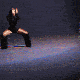 a woman in a black bodysuit is dancing on a stage with her hand in the air
