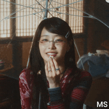 a woman wearing glasses is eating popcorn under an umbrella with ms written on the bottom right