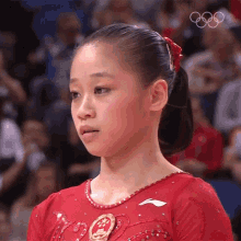 a girl in a red dress with the olympic rings in the background looks at the camera