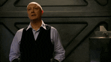 a bald man wearing a black vest and a blue shirt