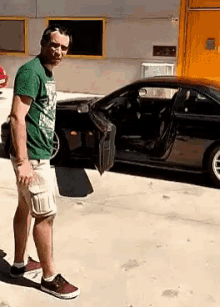 a man in a green shirt stands in front of a black car