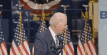 a man in a suit and tie is standing in front of a microphone in front of a wall of american flags .