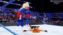 a woman is laying on the floor in a wrestling ring while two women are standing behind her .