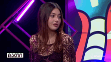 a woman in a lace top is standing in front of a screen that says aroon