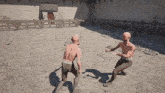 two bald men are fighting in a sandy area with a wooden fence in the background