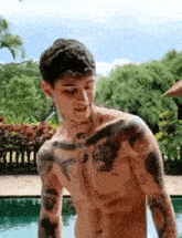 a shirtless man with tattoos on his chest and arms is standing next to a pool .