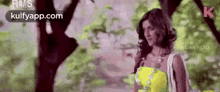 a woman in a yellow dress is standing in front of a tree .