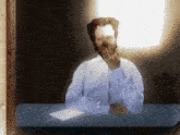 a man in a white shirt is sitting at a desk with his hand on his chin