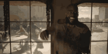 a man with a beard is standing in front of a window with a crowd behind him