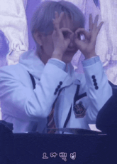 a man in a white jacket and tie is making a heart with his hands