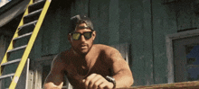a shirtless man wearing sunglasses and a hat stands in front of a building