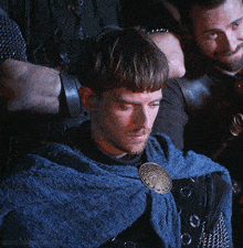 a man wearing a blue cape with a gold buckle on it looks down at something