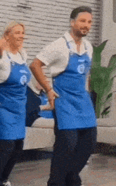 a man and a woman wearing blue aprons are dancing together in a living room .