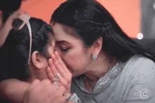 a woman kisses another woman on the cheek with the letters sc visible
