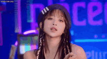 a woman wearing a hat and braids looks at the camera
