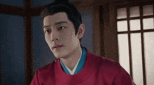a man in a red robe is sitting in a room looking at the camera .