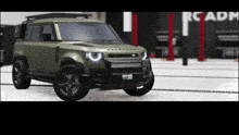a green land rover defender is parked in front of a garage