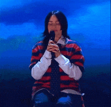 a woman in a striped shirt and tie is holding a microphone .