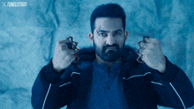 a man with a beard is holding a pair of knuckle dusters in front of a blue background that says toms 2005