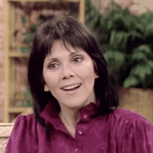 a woman in a purple shirt is sitting on a couch and smiling .