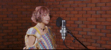 a woman is singing into a microphone in front of a brick wall in a recording studio .
