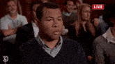 a group of people are sitting in a room with a red sign that says live
