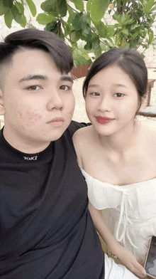 a man and a woman are posing for a picture in front of a tree .
