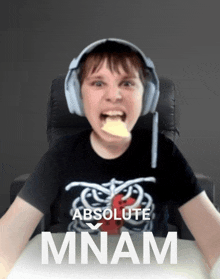 a boy wearing headphones and a shirt that says absolute mnam holds a piece of food in his mouth