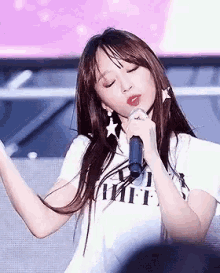 a woman is singing into a microphone while wearing a white shirt and earrings .