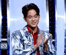 a young man in a denim jacket applauds in front of a screen with the number 23 on it
