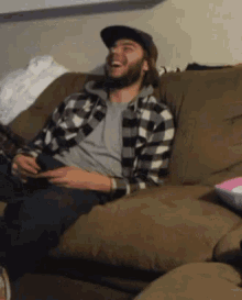 a man sitting on a couch wearing a plaid shirt and hat