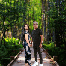 a man and woman standing on a wooden bridge in the woods