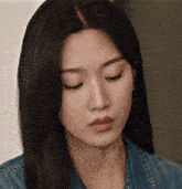 a close up of a woman 's face wearing a denim jacket and looking down .