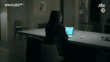 a woman is sitting at a table with a laptop and a jtbc logo in the background .