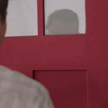 a man is standing in front of a red door with a shadow of a person behind it .