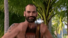 a shirtless man with a beard is standing in front of a palm tree in the jungle .