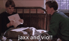 two young men are sitting on a bed talking to each other and one of them is reading a piece of paper .