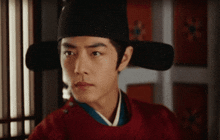 a man wearing a black hat and a red shirt looks at the camera