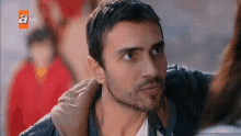 a man with a beard is looking at a woman with a tv logo behind him