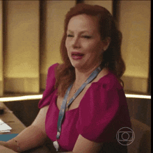 a woman in a pink shirt is sitting at a desk with her mouth open .