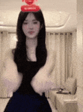 a woman in a black dress with a red heart on her head is standing in a living room .