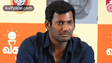 a man in a blue shirt is sitting in front of an orange wall with the words kulfyapp.com on the bottom