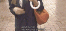 a woman is holding an umbrella and a purse while walking down a sidewalk .