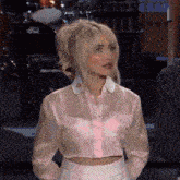 a woman is wearing a pink crop top and white skirt .